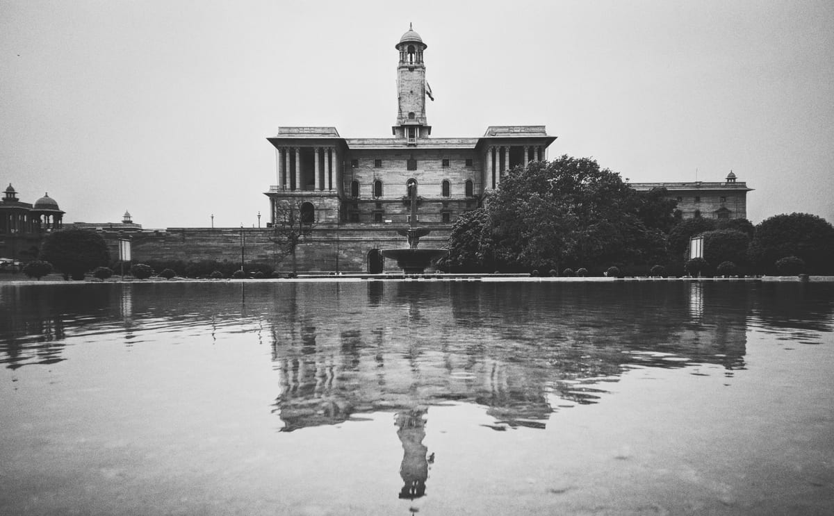 Grayscale photo of a historic building reflecting on water in New Delhi.