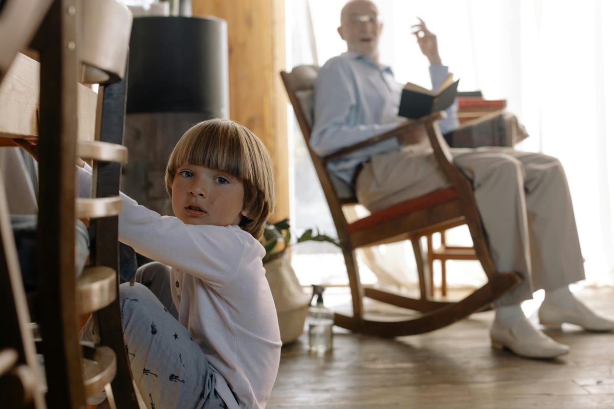 A young boy sitting on the floor with his grandfather in a rocking chair, enjoying a quiet moment indoors.