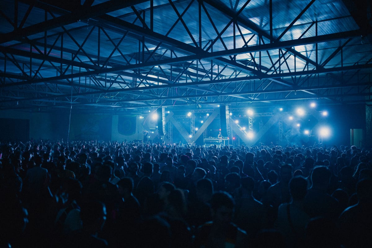 A vibrant indoor concert with a large energetic crowd enjoying the live performance.