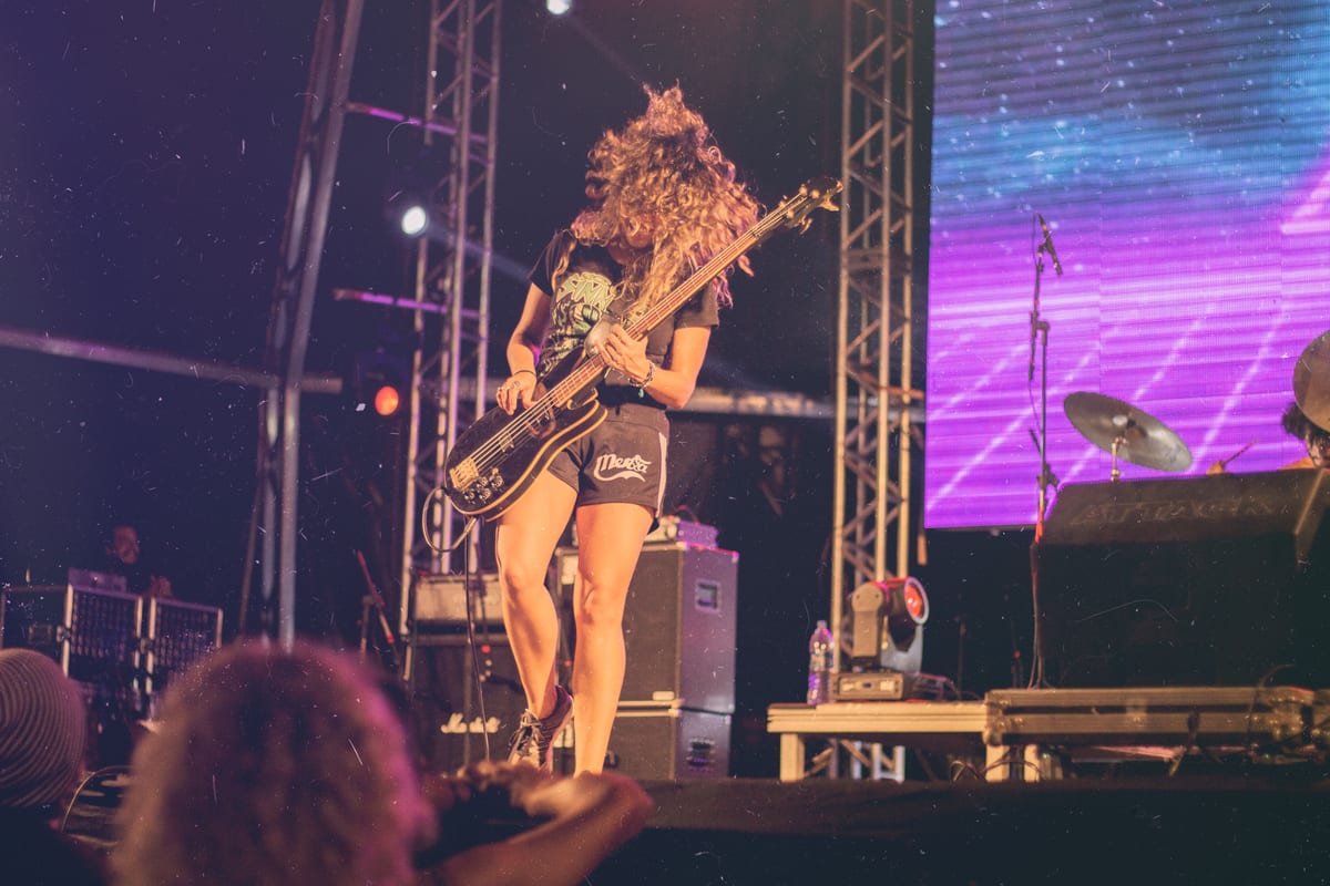 Dynamic live performance with a female bassist energizing the crowd under vibrant stage lights.