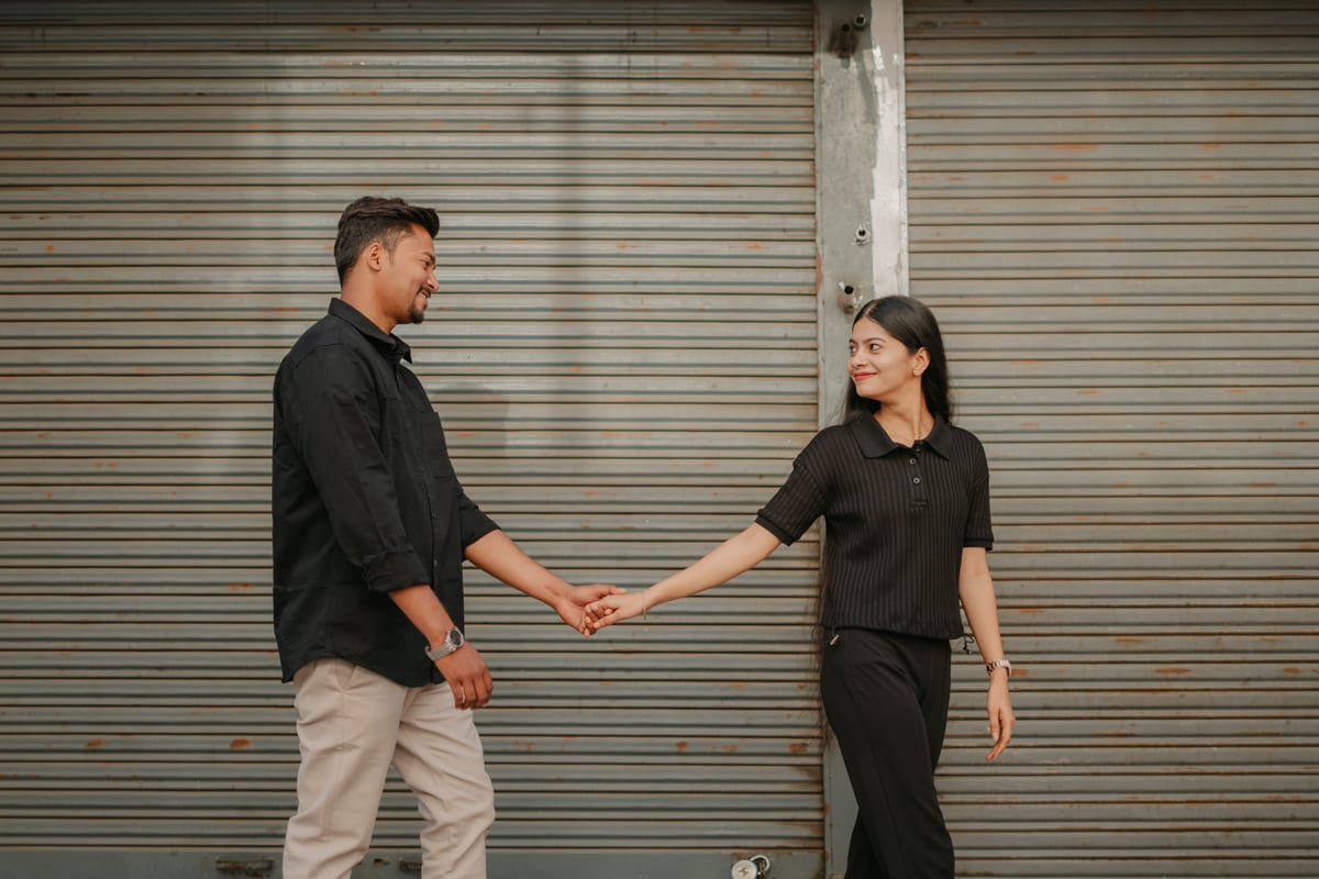 Young couple holding hands and smiling in front of a metal shutter, conveying connection and love.