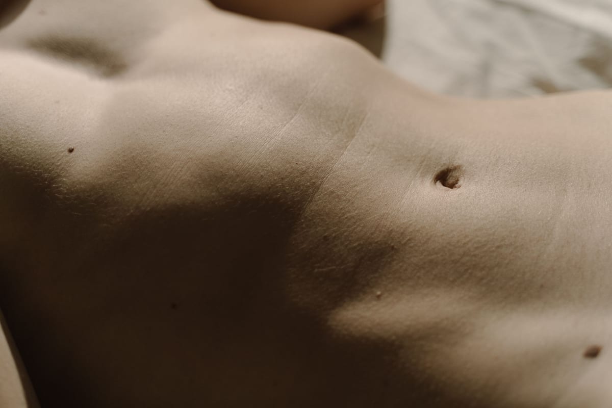 Detailed close-up of human skin featuring belly button, texture, and moles under natural light.