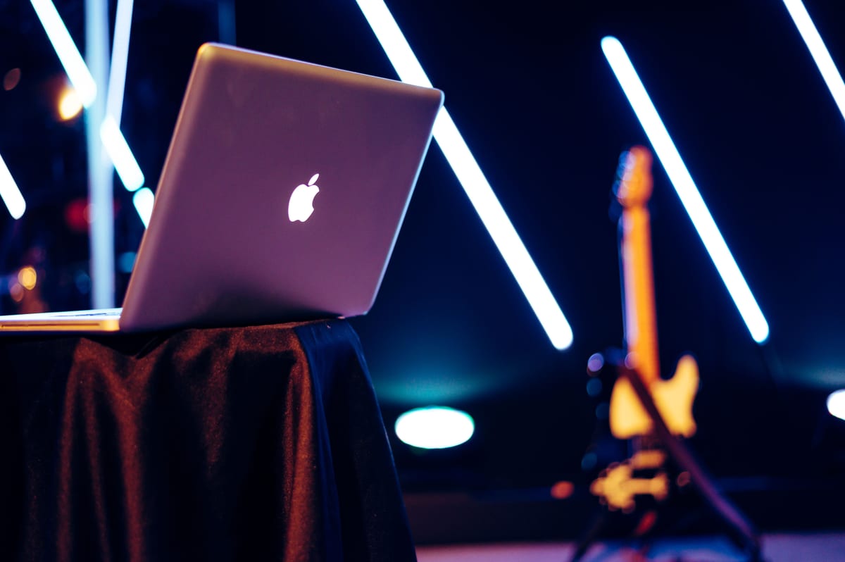 A sleek laptop sits on a table with vibrant neon lights and a guitar in the background.