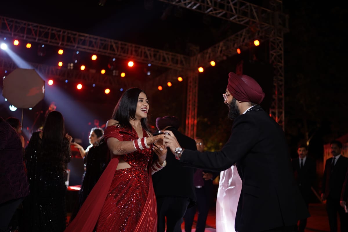 A lively moment at an Indian wedding with a couple dancing energetically amidst guests under glowing lights.