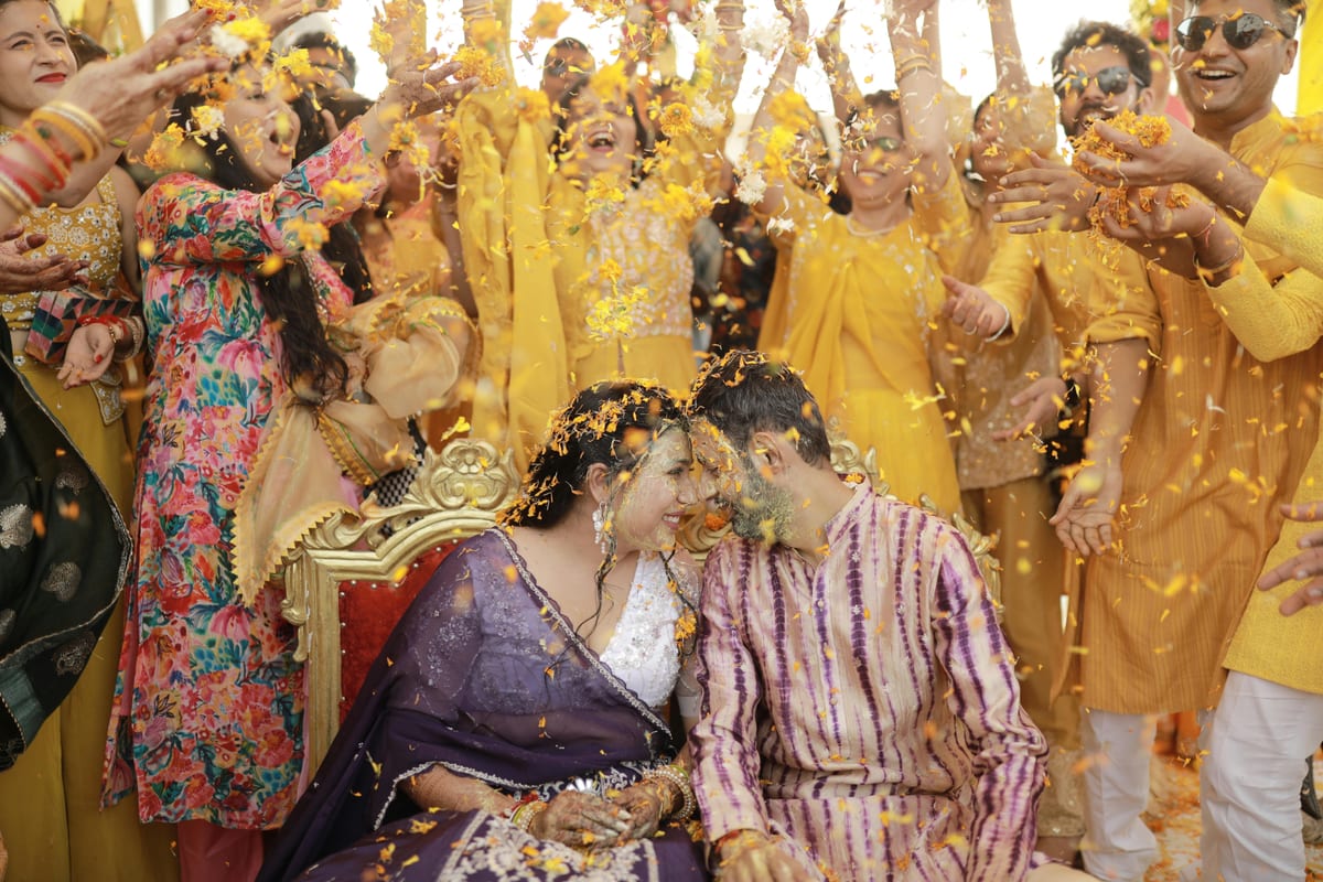 Indian couple joyfully participates in a vibrant Haldi ceremony surrounded by friends and family.
