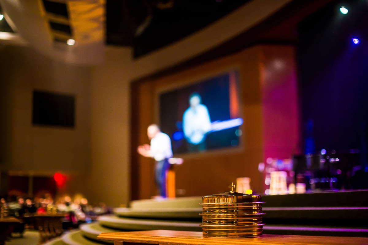 A conference scene with a blurred speaker and microphone on stage lighting.