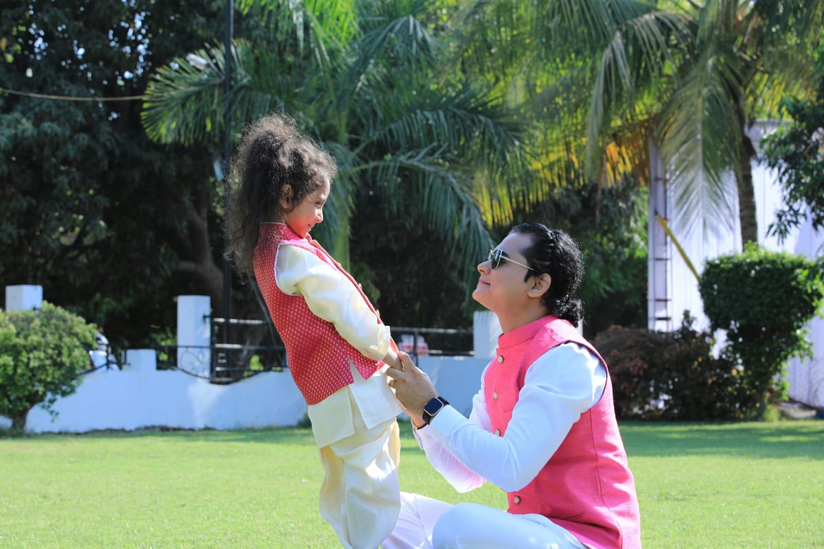 Father and child enjoying a playful moment outdoors in vibrant traditional attire.