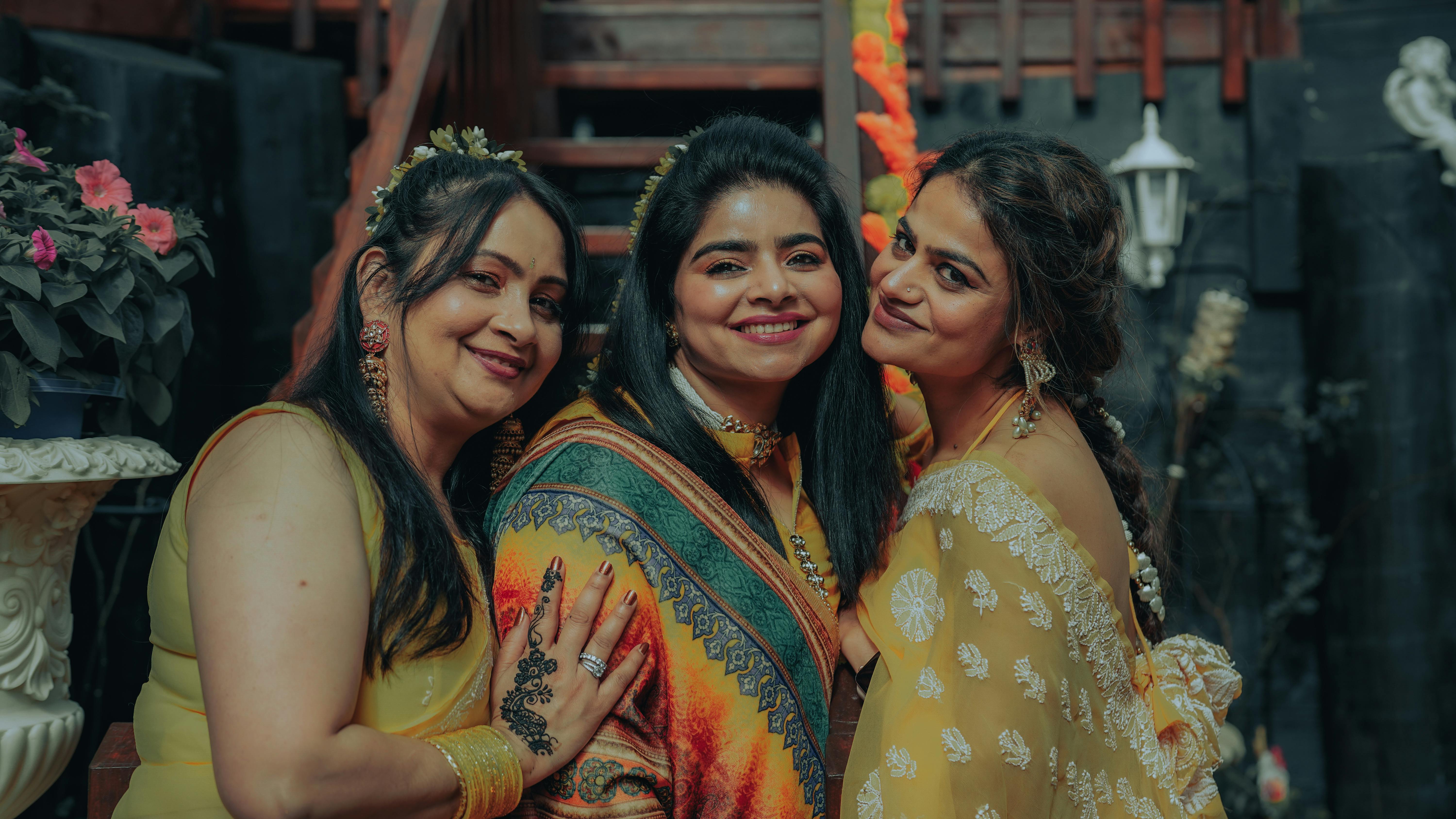 Three women smiling in vibrant traditional clothing, celebrating together indoors.