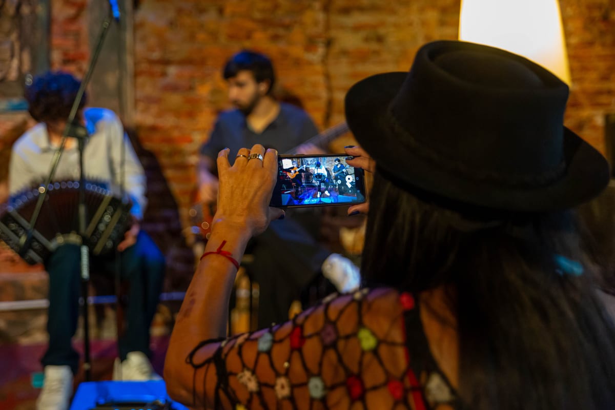 A woman photographs a live band performance in a cozy indoor setting in Mar del Plata, Argentina.
