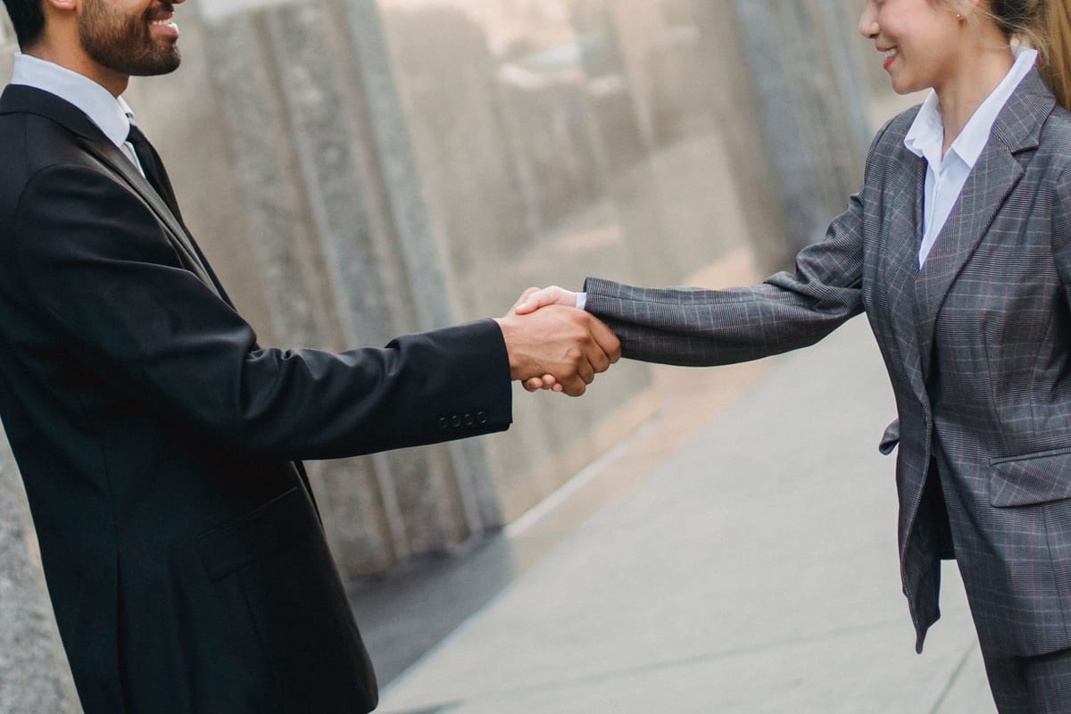 Man and woman in business attire shaking hands outdoors.