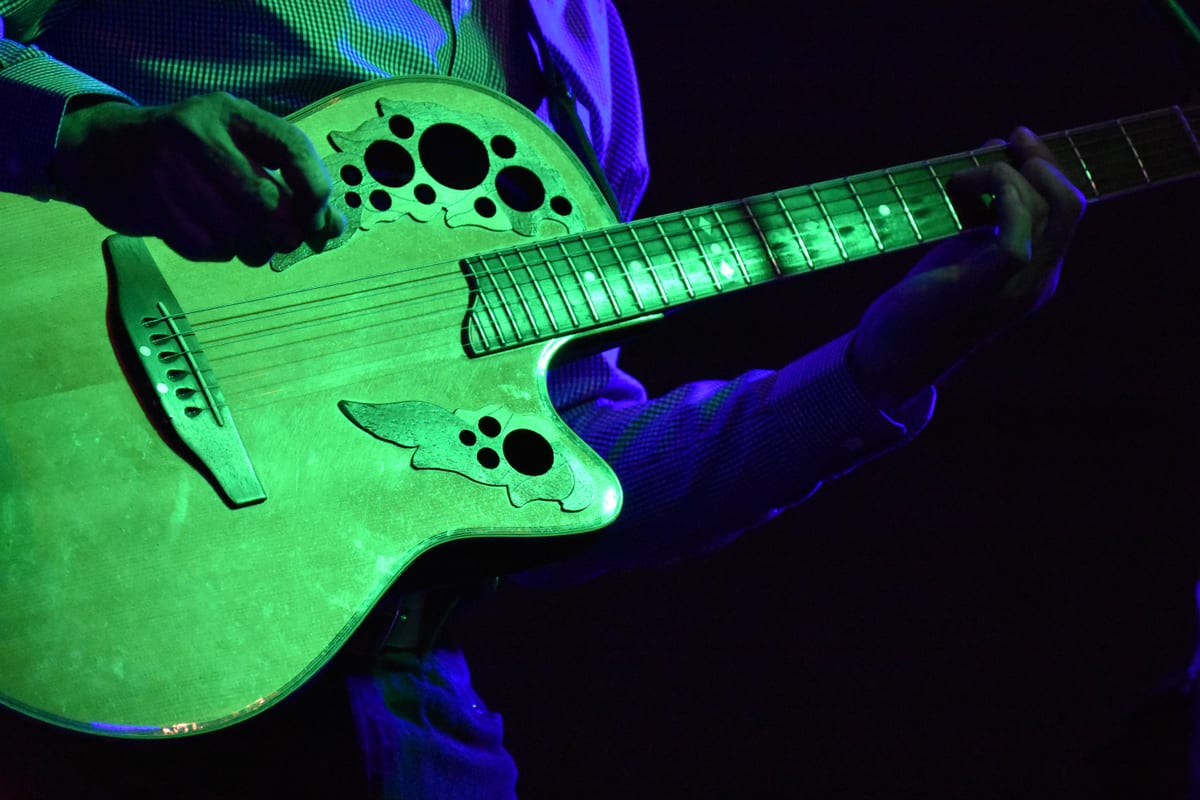 A close-up view of an acoustic guitar being played by a musician under green stage lights.