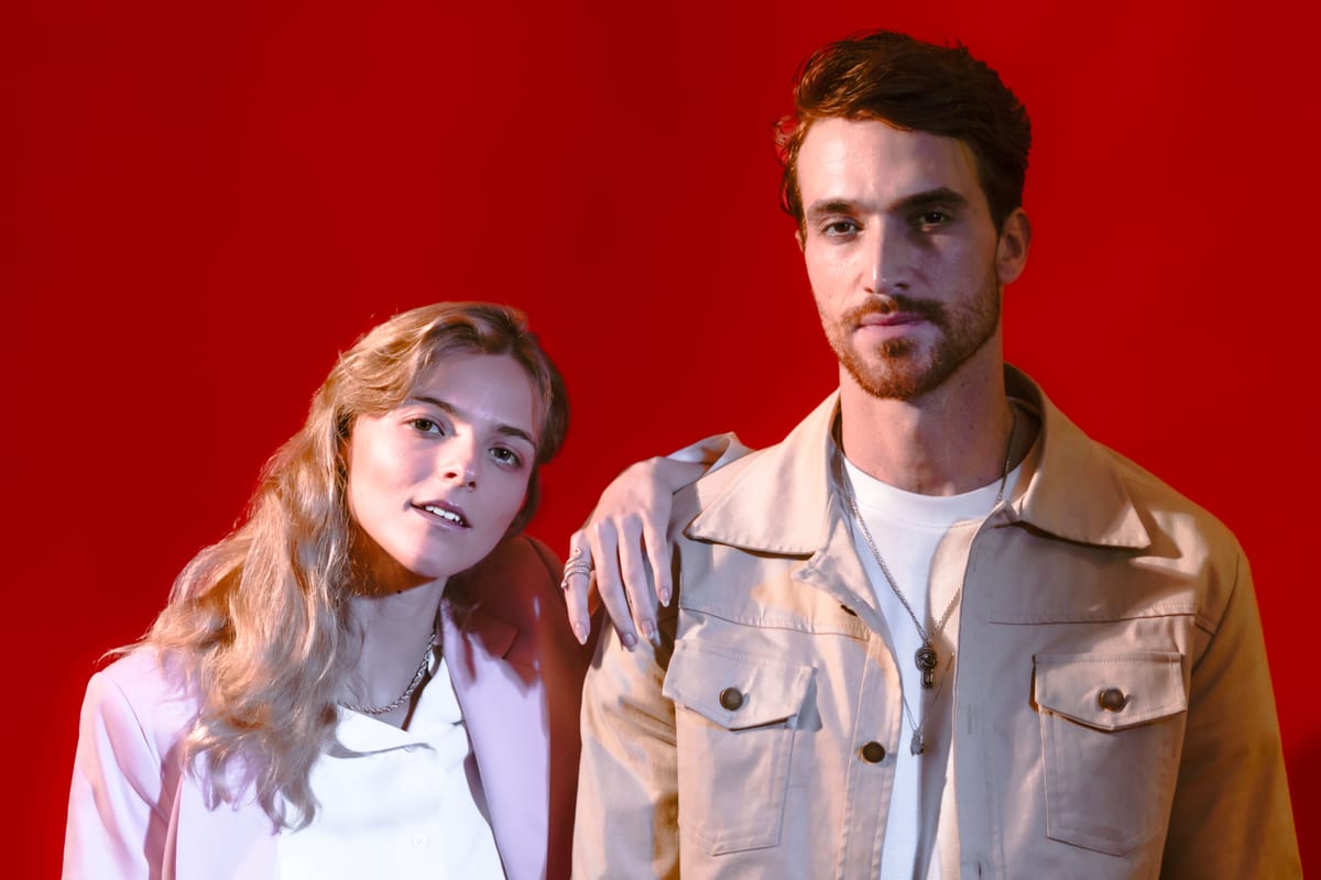 Fashionable couple in stylish attire posing confidently with a bold red background.