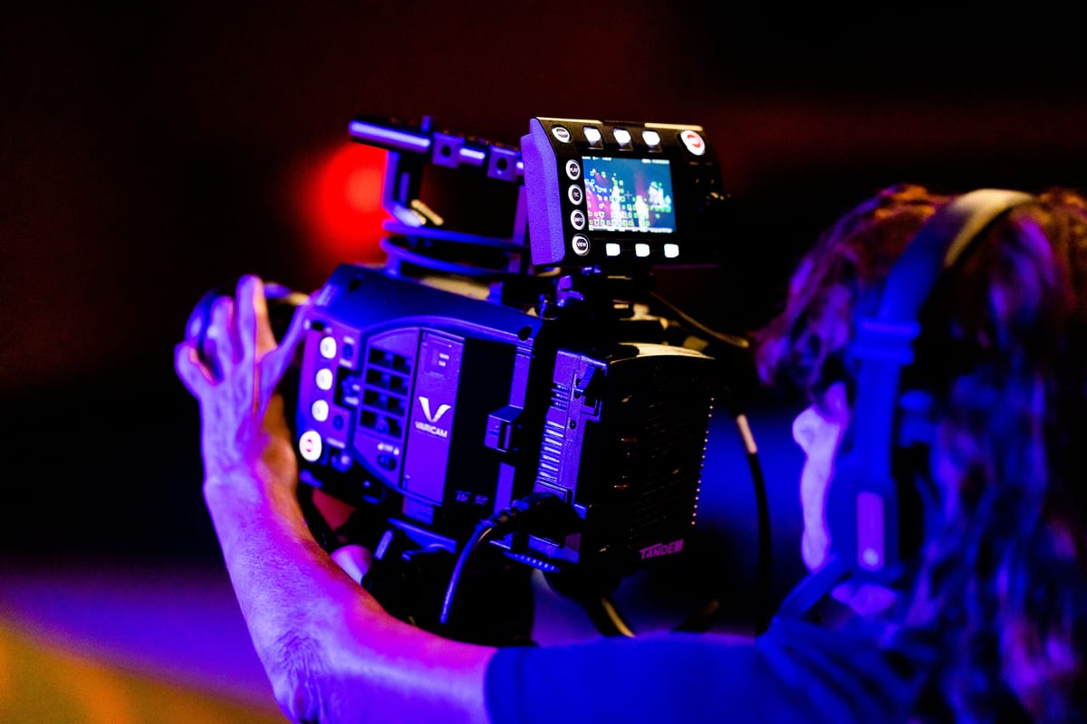 Camera operator working with professional equipment in a dimly lit TV studio setting.