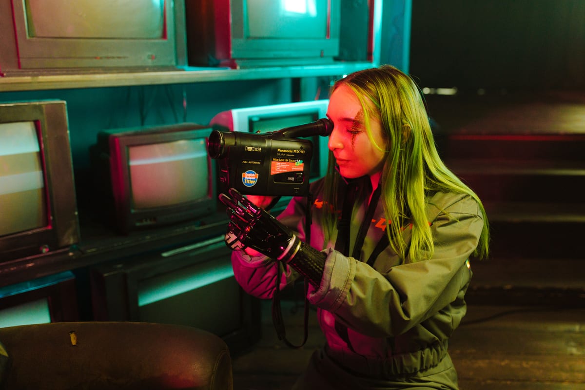 Woman using a prosthetic hand records video indoors, surrounded by vintage TVs.