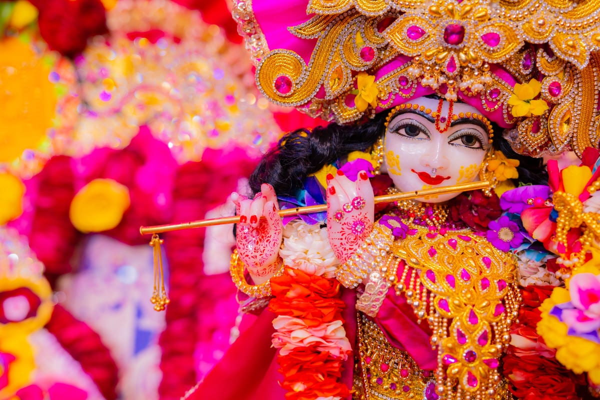 Vibrant Krishna idol adorned with intricate jewelry and flowers holding a flute.