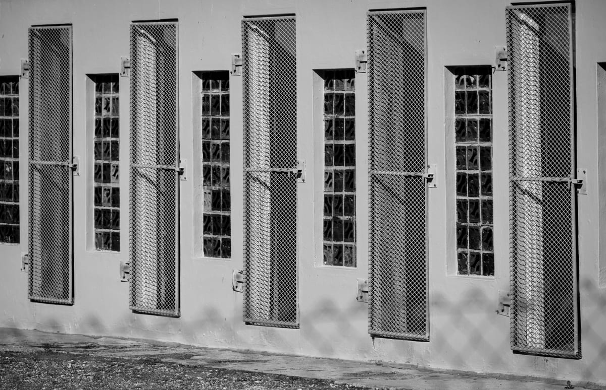 Monochrome image of barred windows on a building, depicting confinement and security.