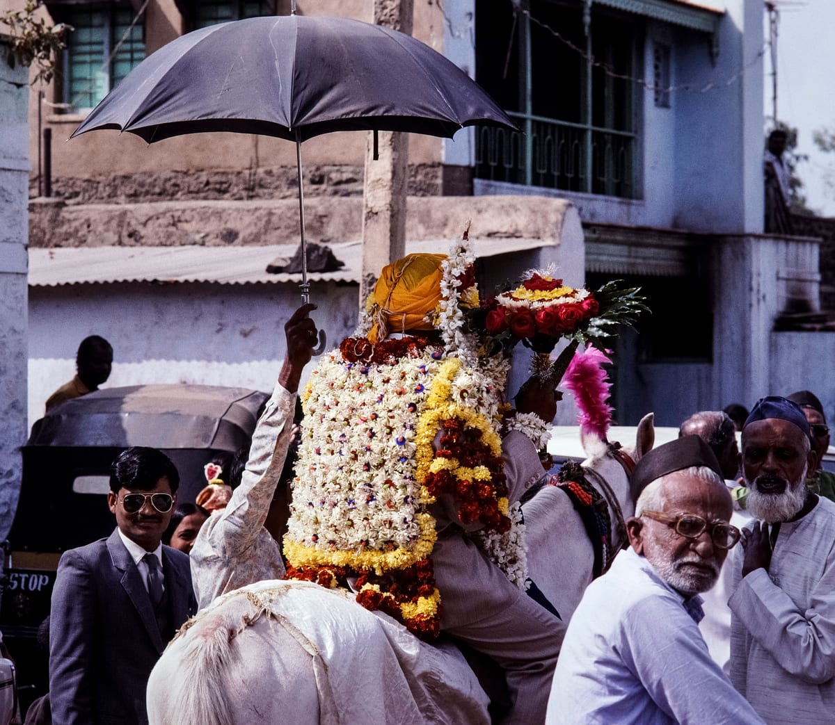 A lively Indian wedding procession featuring a flower-adorned horse and traditional attire, captured in a vibrant street scene.