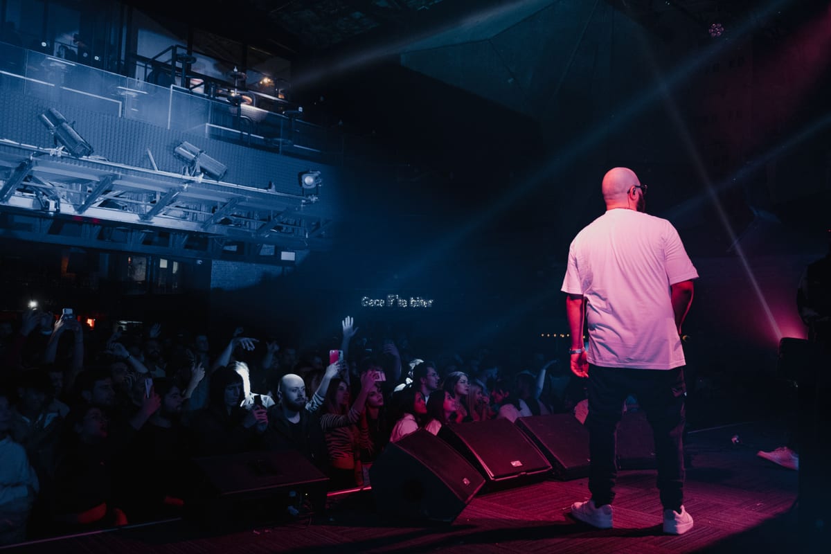 Rapper performing live on stage with vibrant lighting and engaged audience in a concert setting.