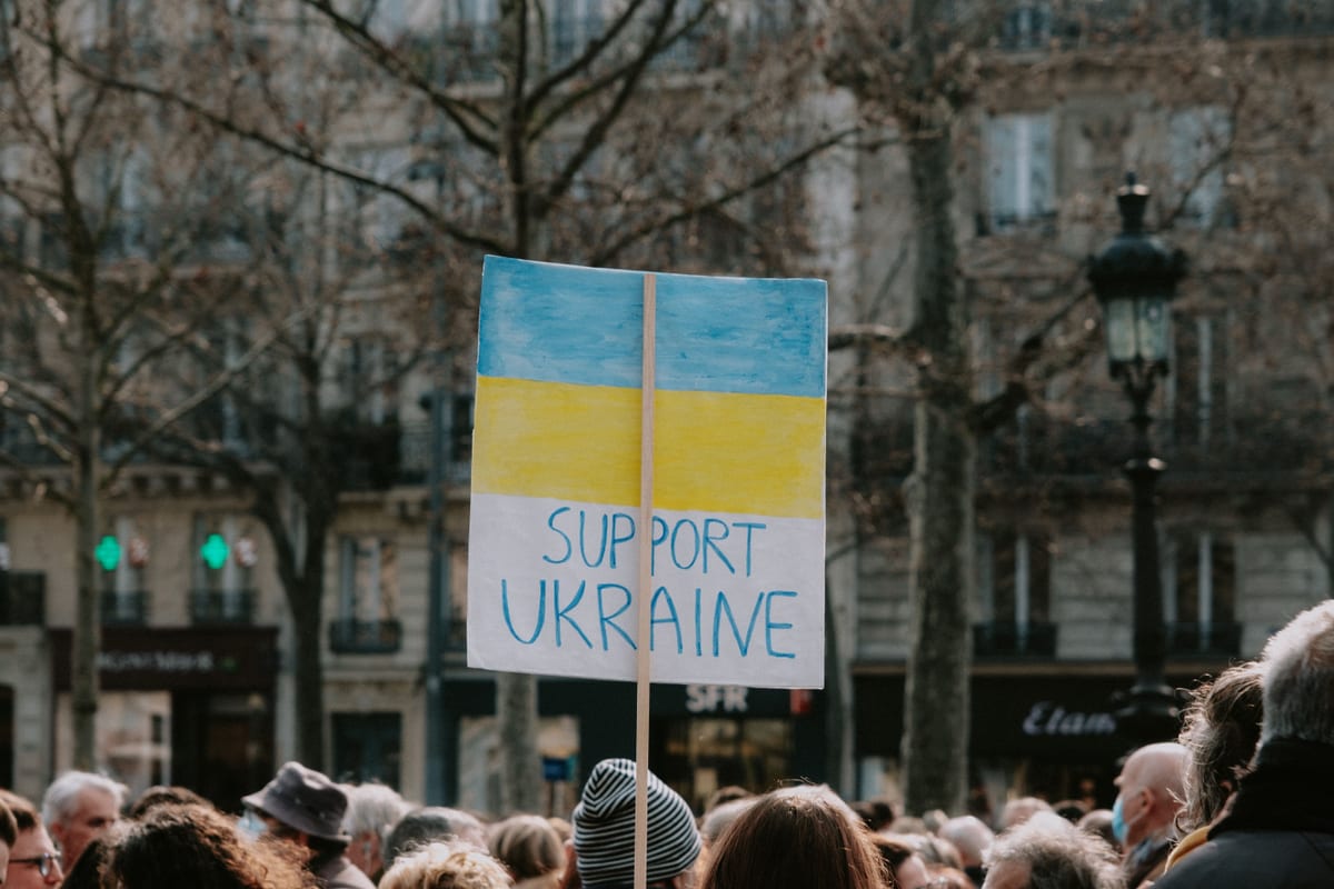 Crowd holding a 'Support Ukraine' banner during an outdoor solidarity rally.