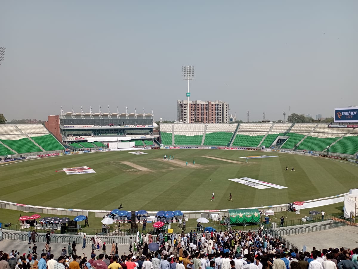 Vibrant cricket match at a large stadium filled with enthusiastic spectators under a bright sky.