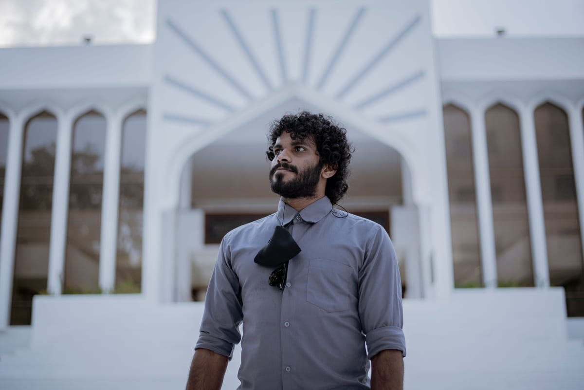 A man with curly hair standing outside a modern building, conveying confidence and style.