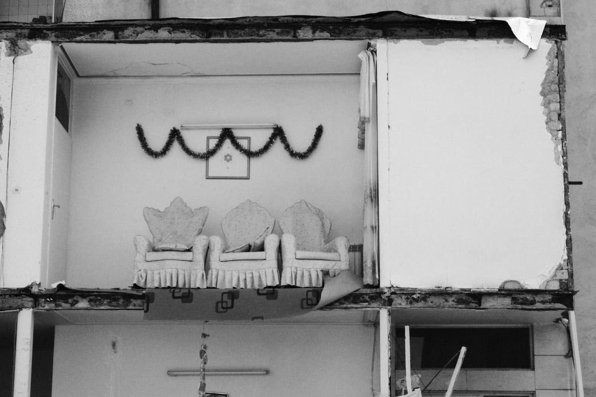 Black and white photo of a room with chairs amid building collapse.
