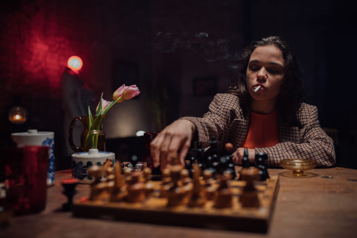 Portrait of a woman smoking and playing chess in a cozy indoor setting.