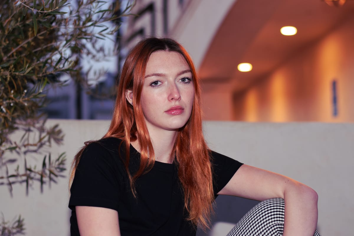 Stylish portrait of a young woman with red hair sitting in West Hollywood during twilight.