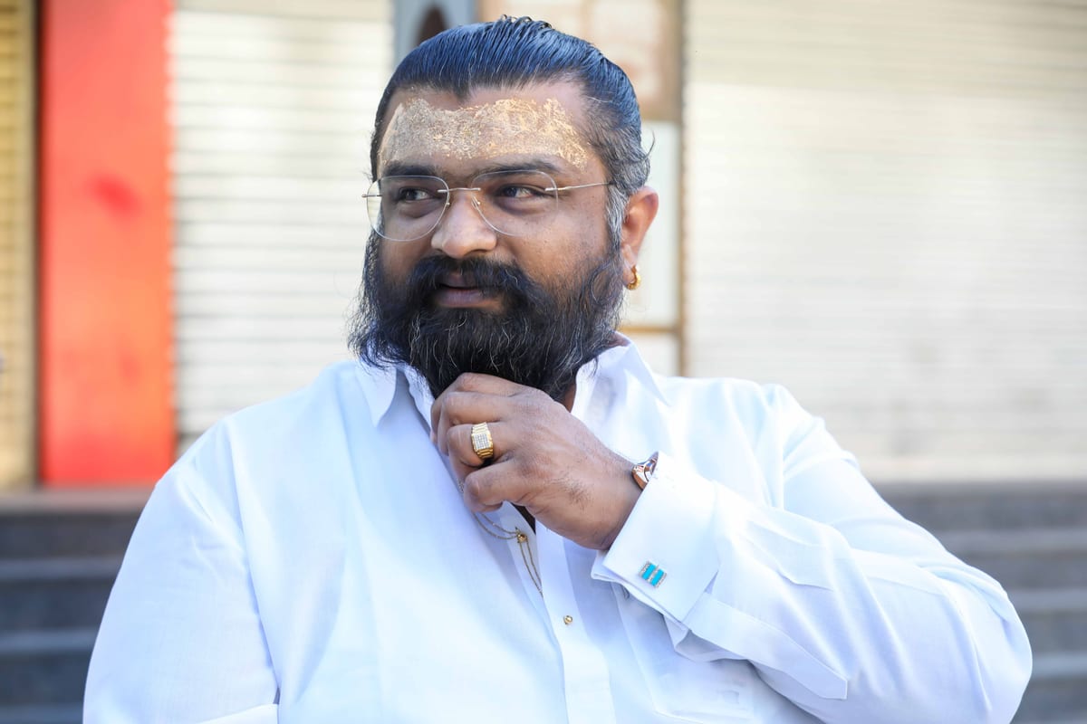 Portrait of a confident adult man with a beard and spectacles, wearing a white shirt outdoors.