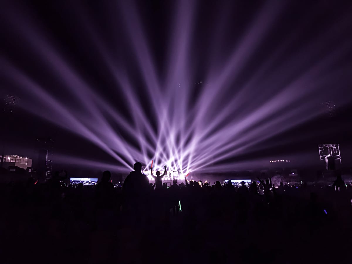 A lively night concert with beams of colorful lights and an energetic crowd.