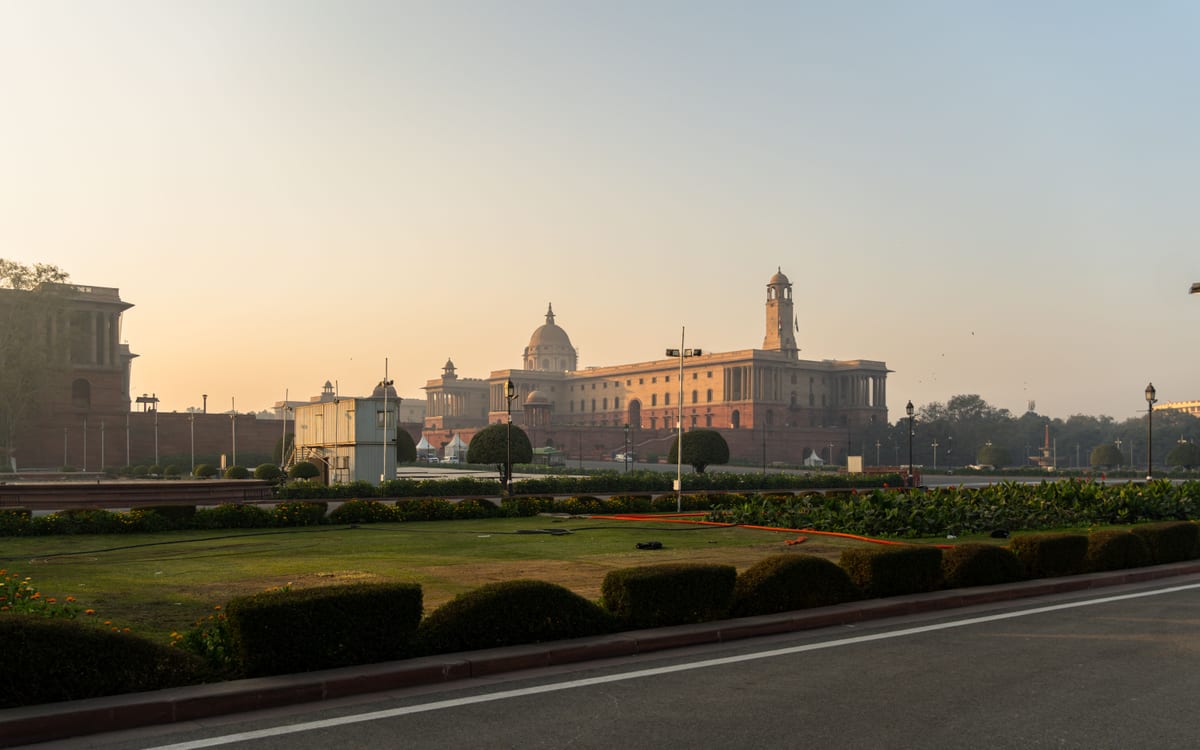 View of Rashtrapati Bhavan in New Delhi with manicured gardens and sunrise sky.