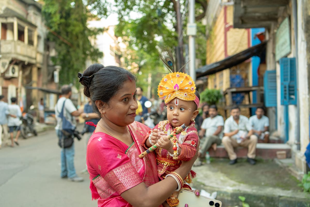 A woman holding her baby dressed in traditional attire during an outdoor festival.