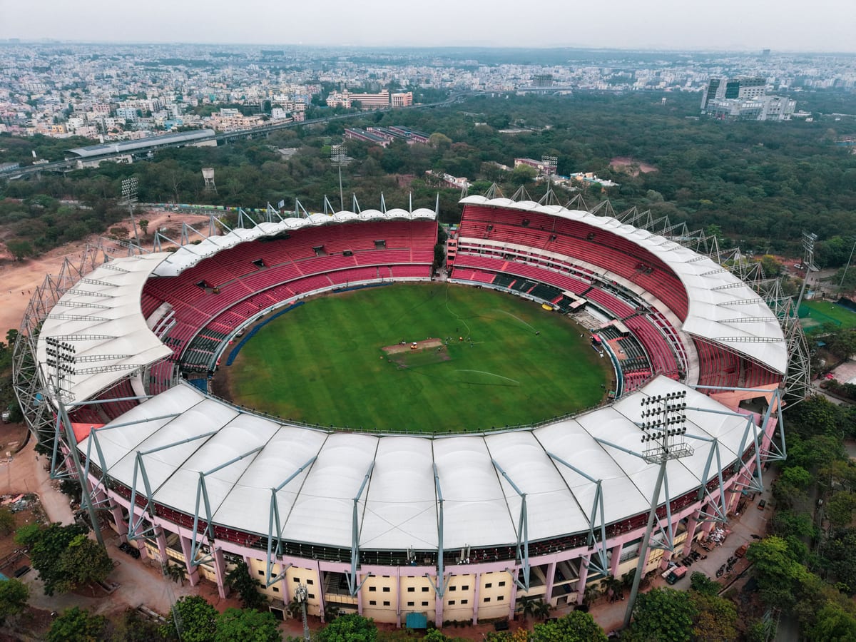 Aerial photograph of a large, empty sports stadium surrounded by greenery and urban landscape.