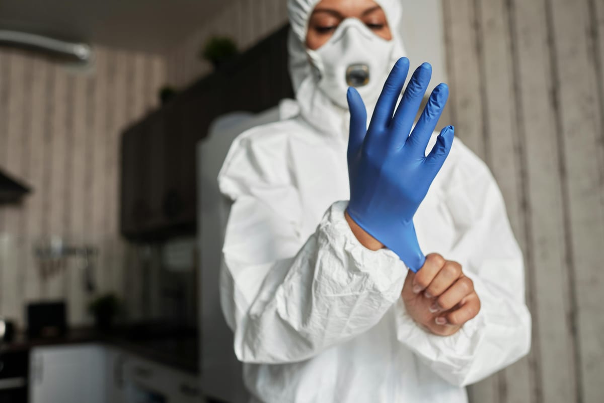 Person in protective suit wearing blue gloves indoors for safety.
