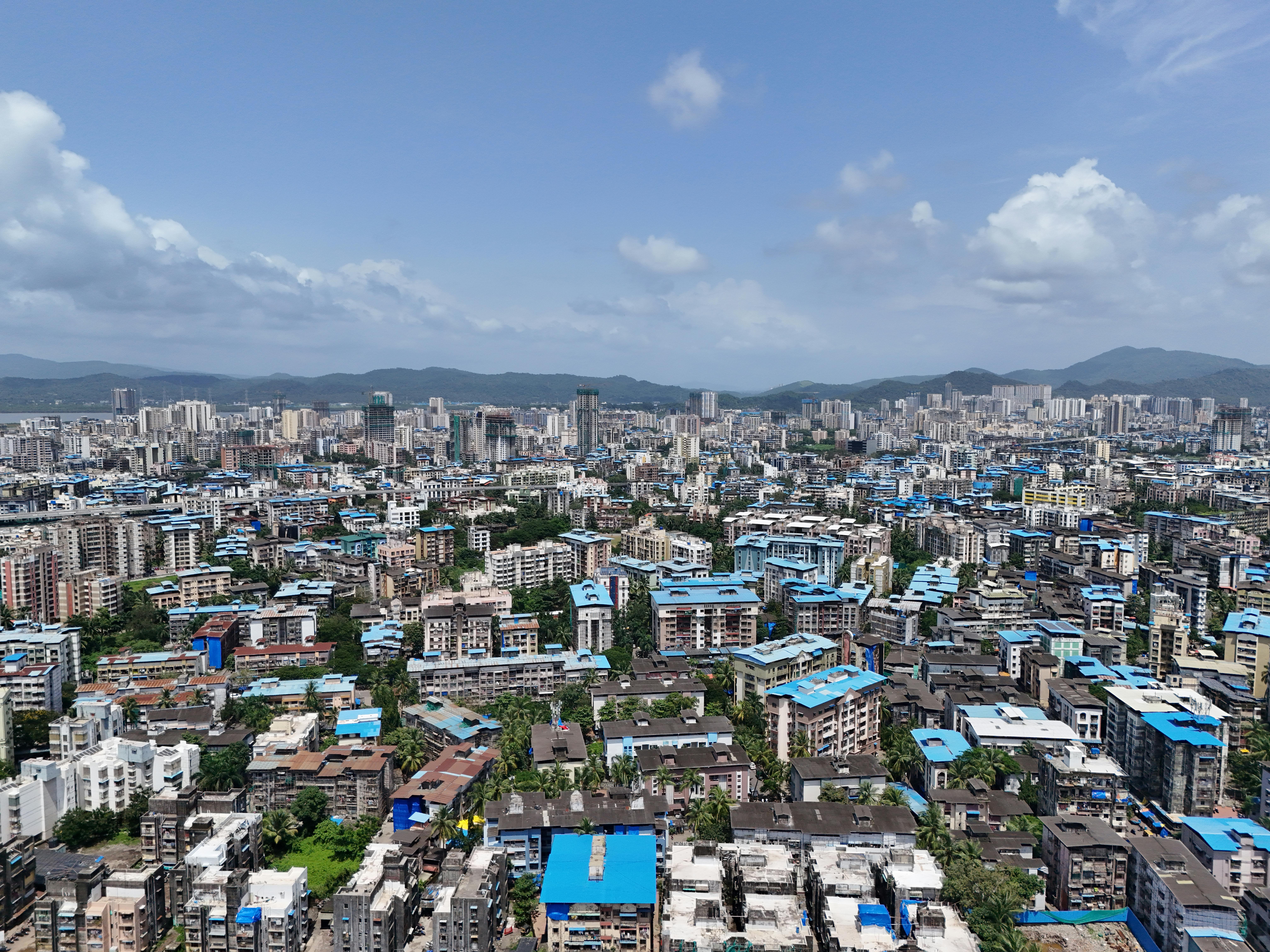A wide aerial shot of Mumbai's skyline featuring distinctive blue rooftops under a clear sky.