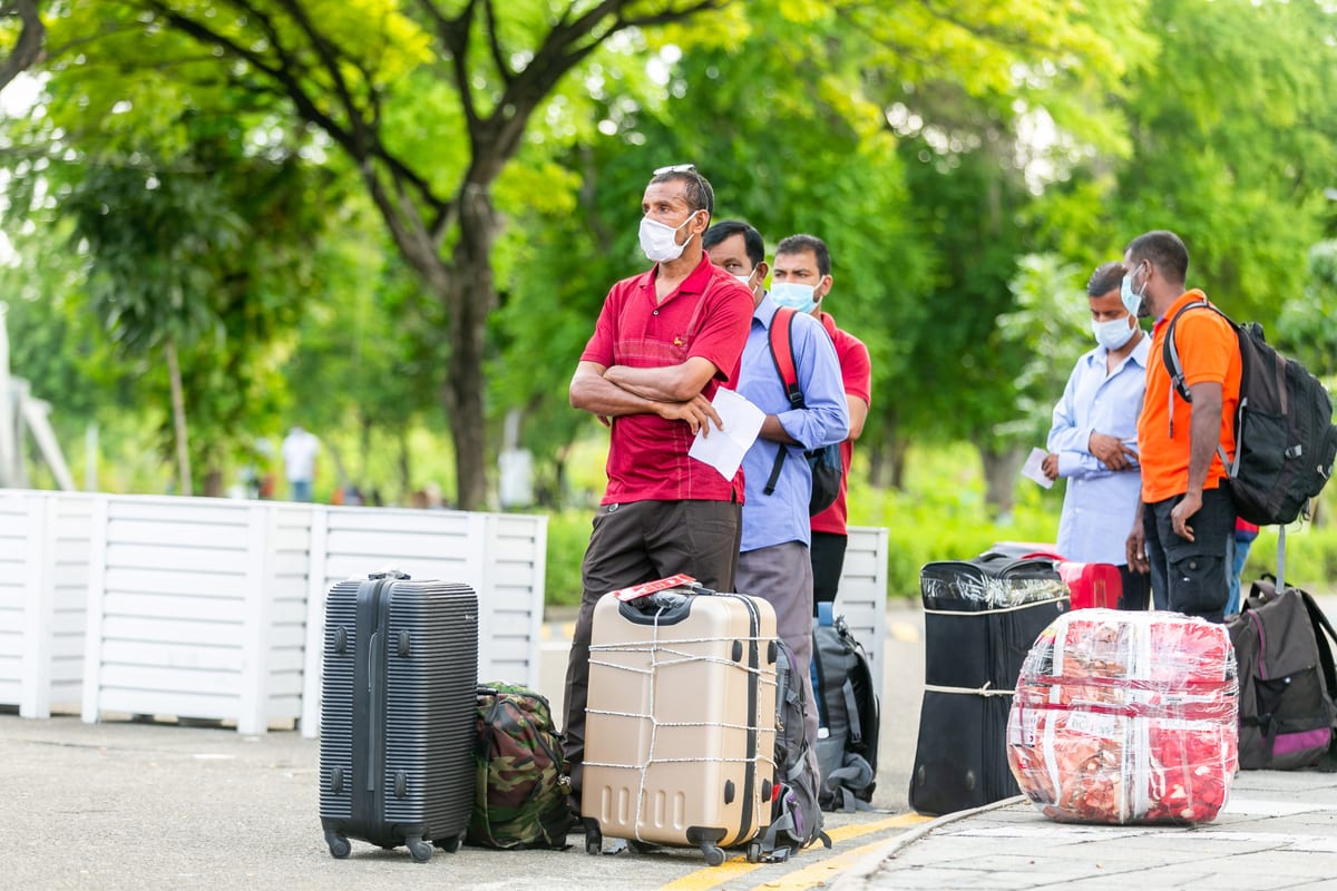 People standing with suitcases wearing masks outdoors, indicative of travel during COVID-19 times.