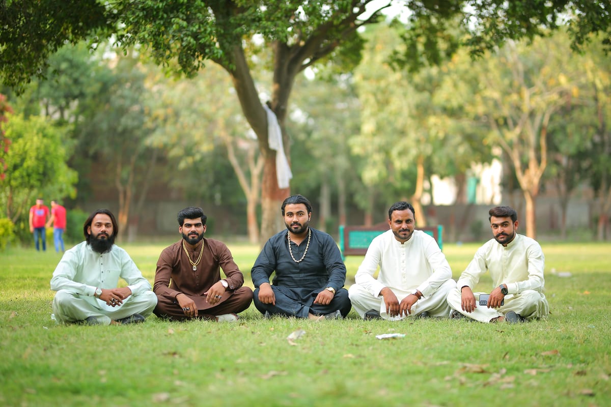 Group of men in traditional attire sitting in a park in Lahore, Pakistan.