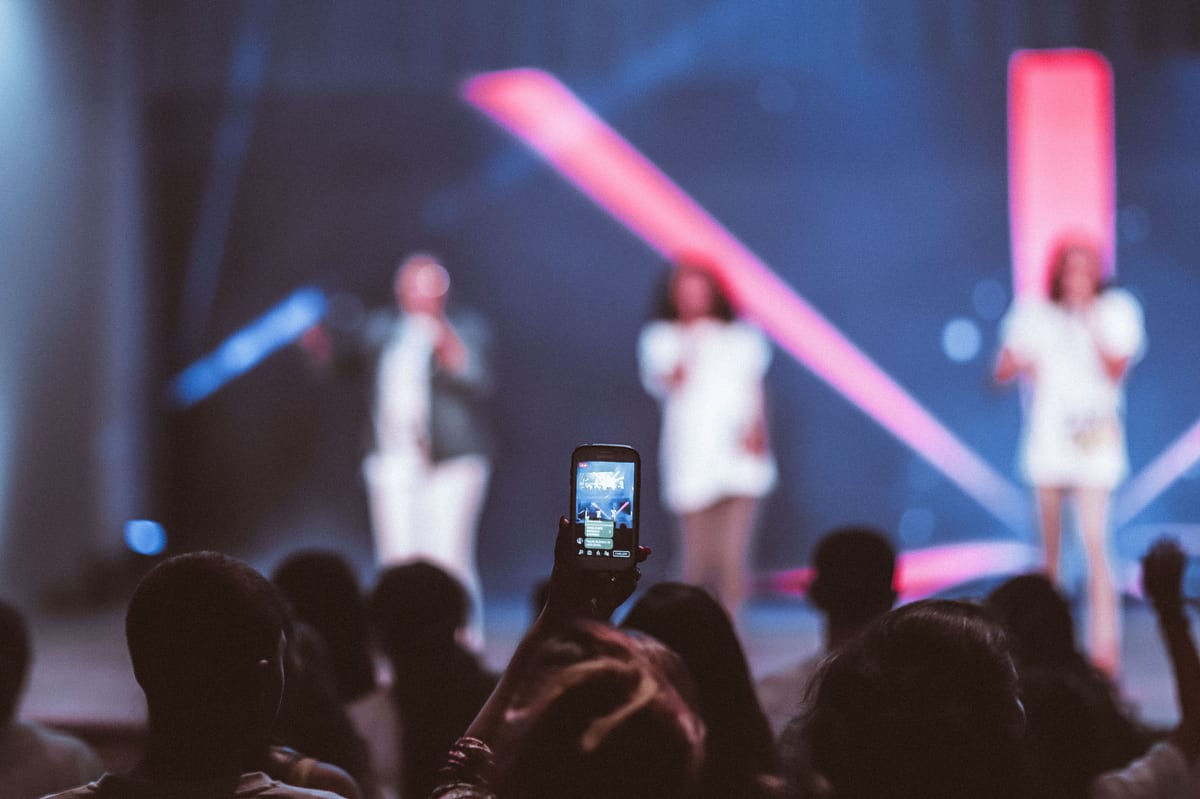 Audience members capture a live music performance on their phones, experiencing vibrant stage lights.
