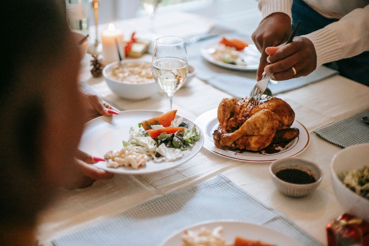 A warm family dinner scene featuring a roasted chicken with sides and wine on a table setting.