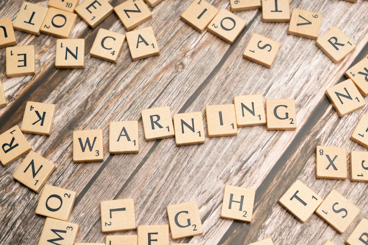 Wooden letter tiles forming the word 'Warning' on a rustic wooden surface.
