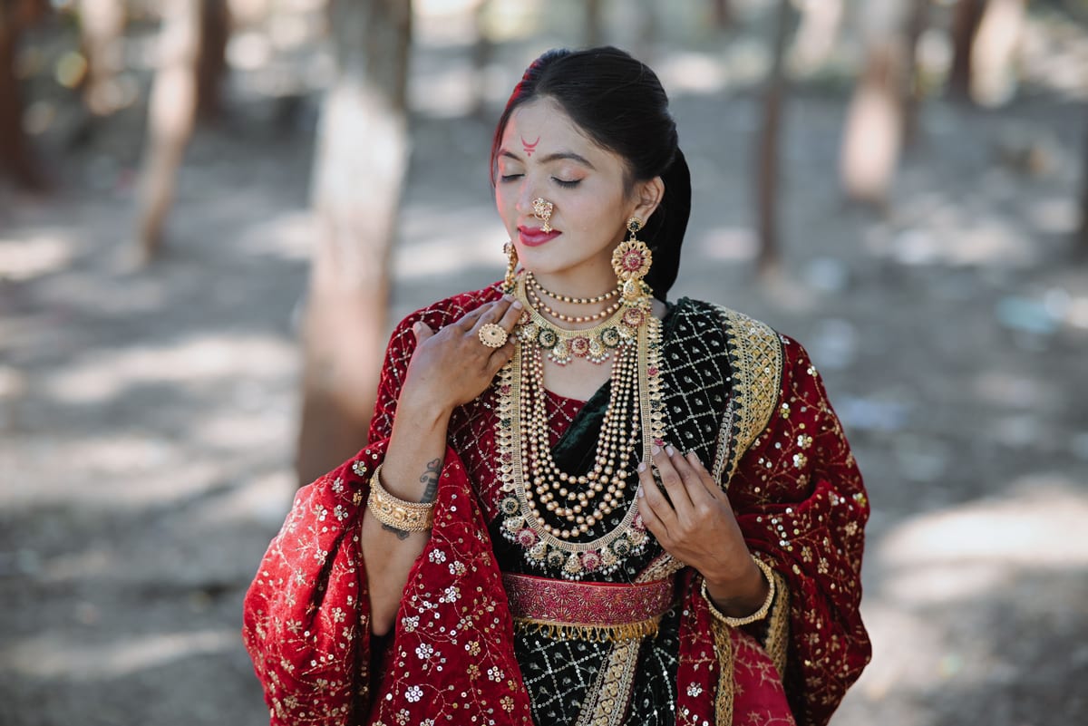 Elegant Indian bride in traditional attire with jewelry, captured in a serene outdoor forest setting.