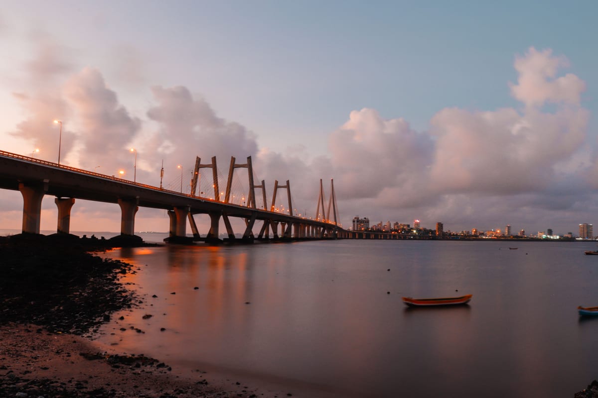 A breathtaking evening view of a bridge extending over calm waters, with city skyline in the background.