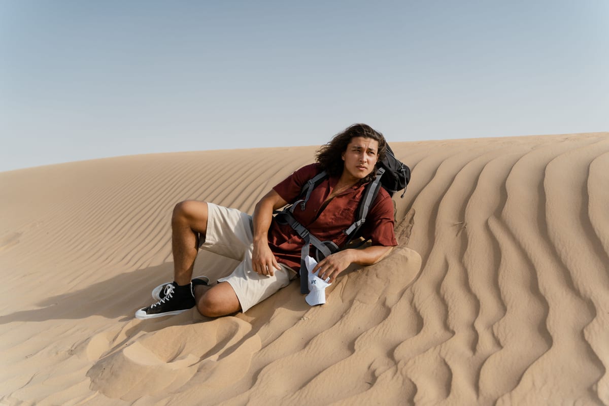 A young man in casual attire relaxes on sand dunes, enjoying a sunny day outdoors.