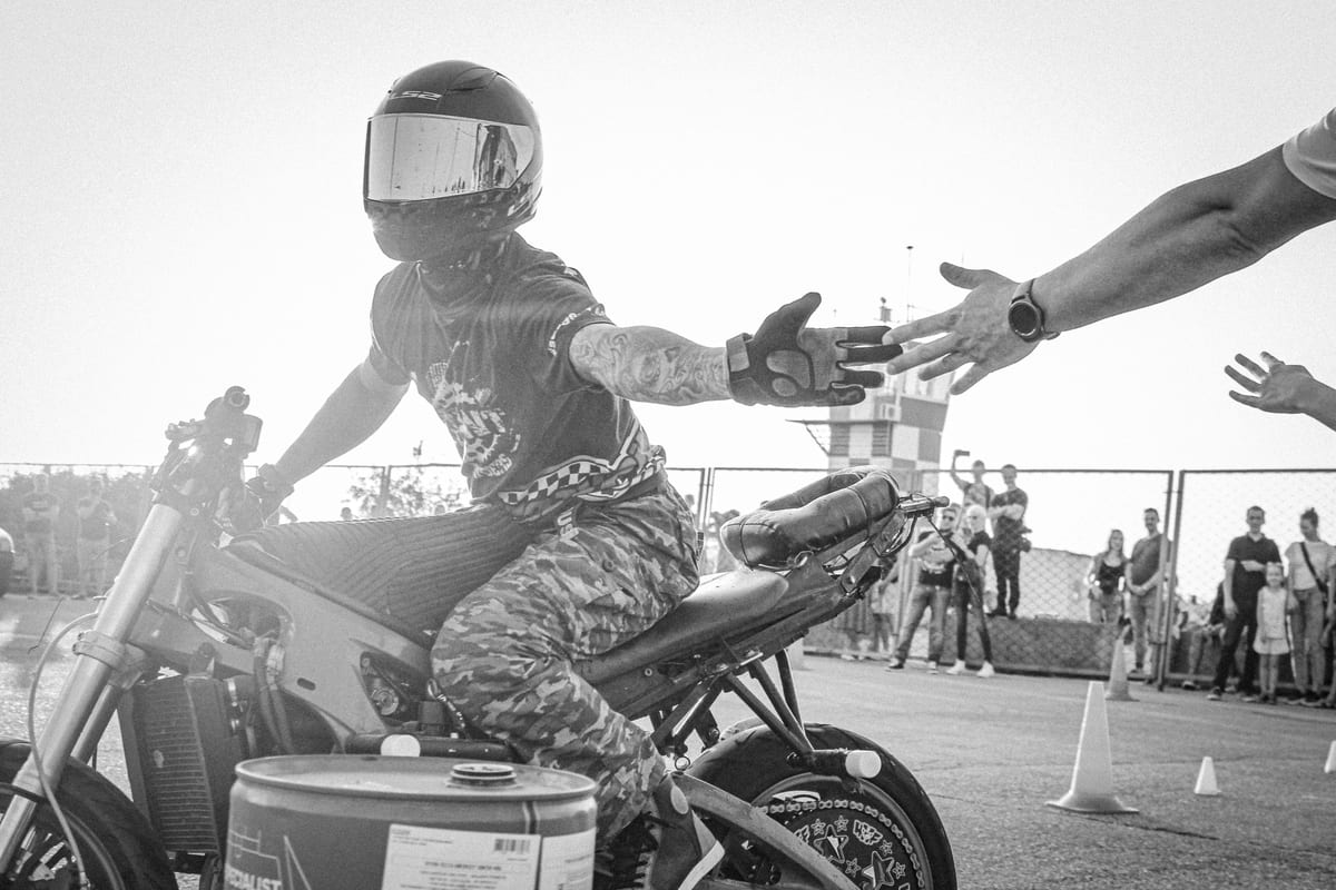 A motorcycle stunt rider high-fives spectators during an outdoor event, showcasing skills and excitement.
