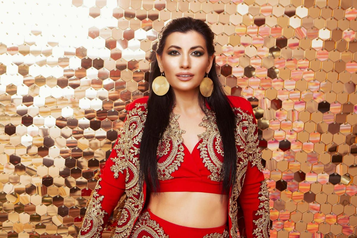 Attractive female wearing red costume and round earrings looking at camera while standing in light studio on background with golden sequins