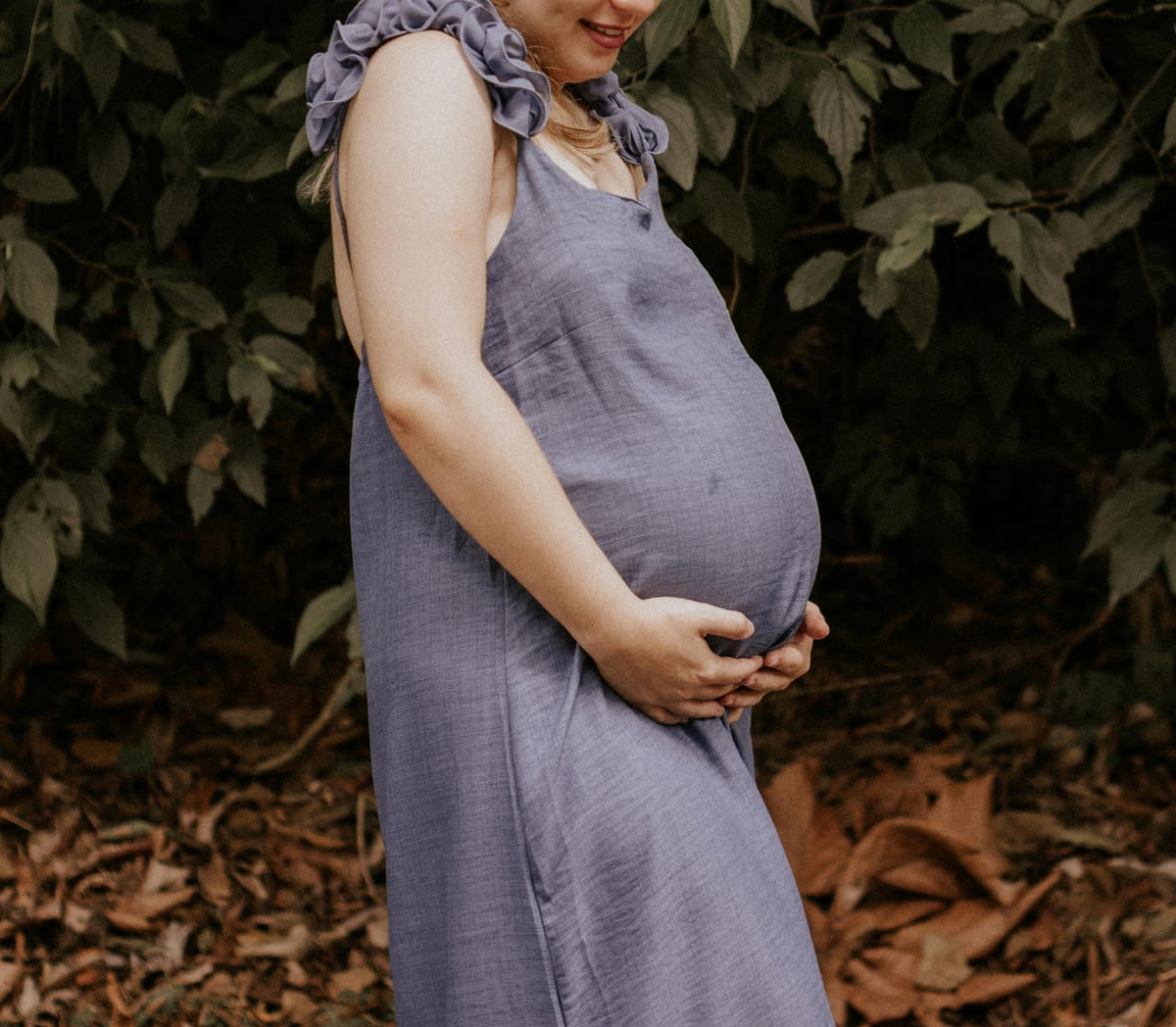 A woman in a blue dress enjoying nature during pregnancy, standing outdoors.
