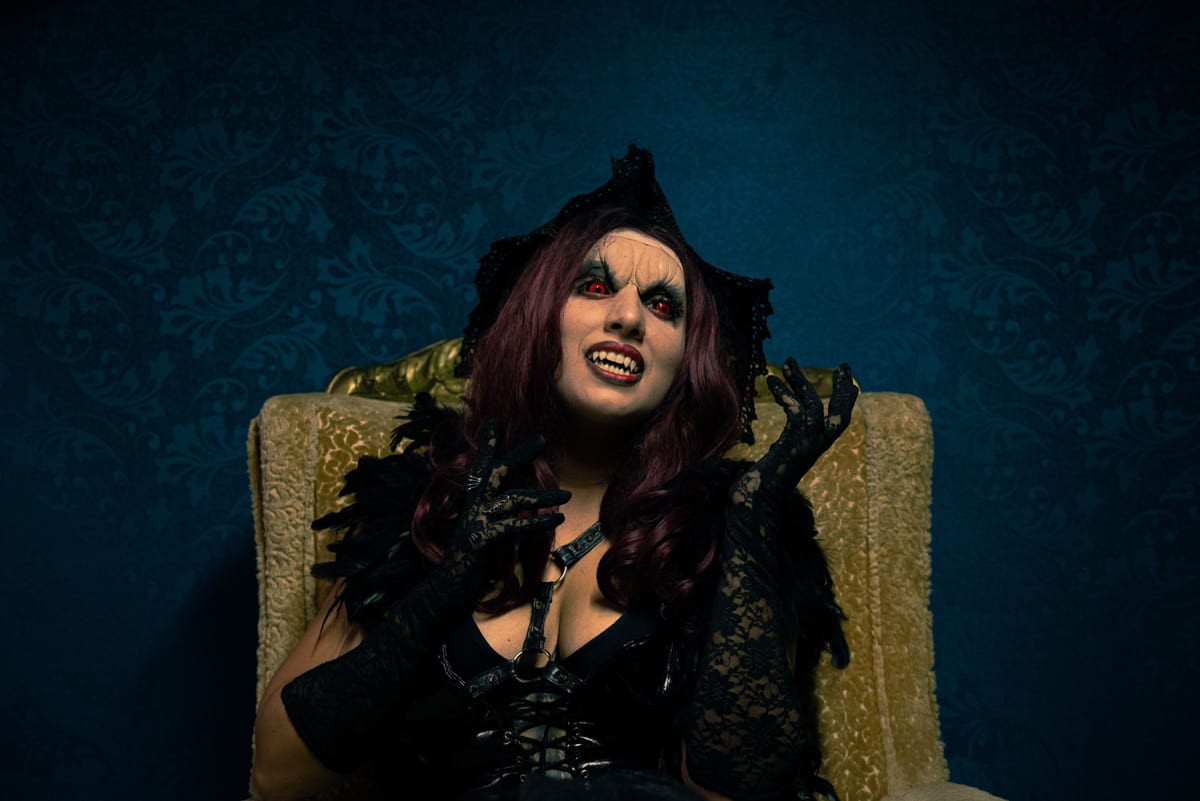 A dramatic portrait of a woman in vampire costume with gothic makeup and attire.