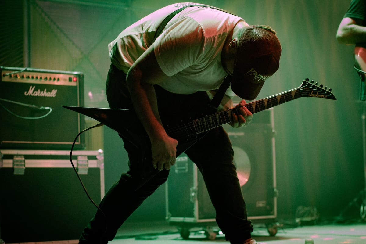 A dynamic guitarist bends forward in a passionate performance on stage with electric guitar and amplifiers.