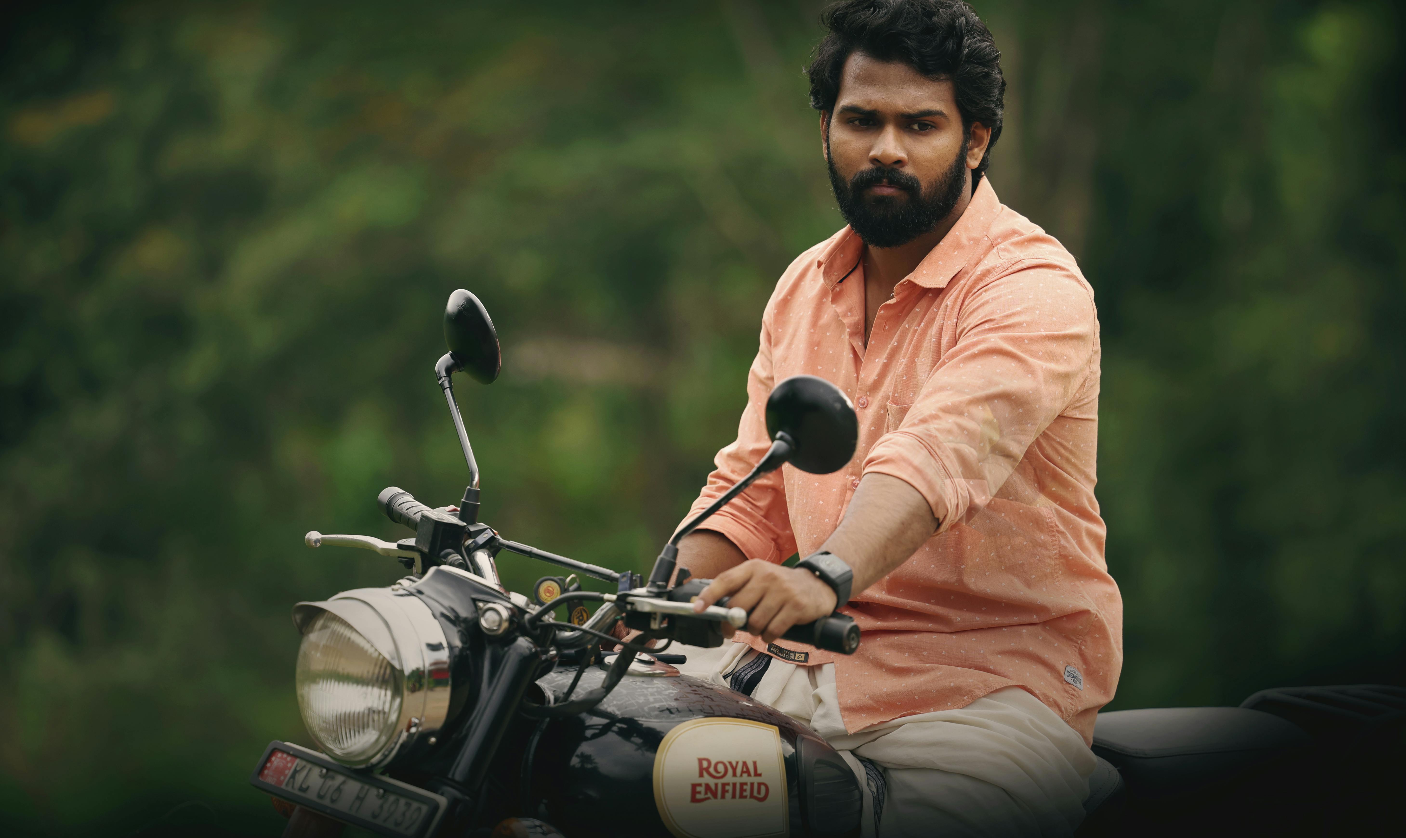Man in pink shirt riding a Royal Enfield motorcycle outdoors, showcasing adventure and freedom.