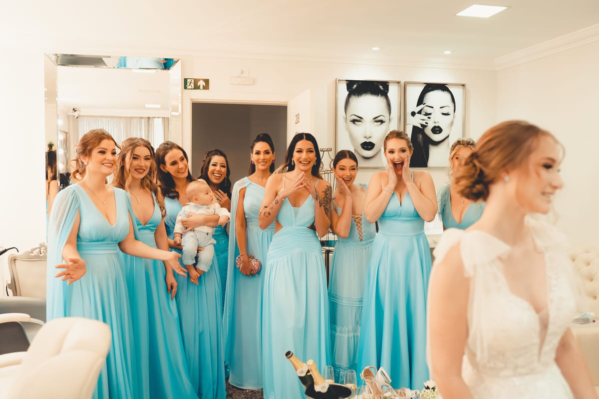 Group of bridesmaids in blue dresses celebrating with the bride indoors.